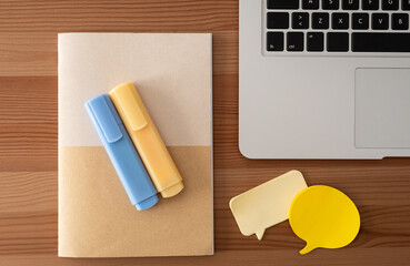 Laptop, yellow notes, blue and yellow markers and notebook. Wood table. Top view.