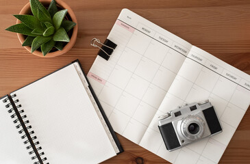 Vintage camera, dotted paper, blank diary and cactus. Wood table. Top view.