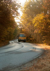 Obraz premium Road with school bus in beautiful autumn forest at sunset.