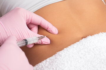A doctor of aesthetic cosmetology makes lipolytic injections to burn body fat on a woman’s...