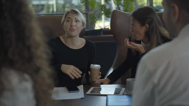Portrait of excited Caucasian woman sitting with coworkers in cafe and talking. Positive successful businesswoman chatting with colleagues in restaurant during break.