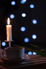 Tea cup on a dark table with candle and bokeh lights in a dark background