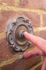 A vintage antique style metal door bell being pushed by the finger of a visitor
