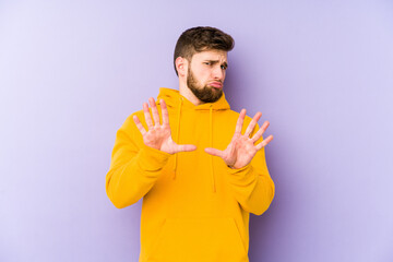 Young man isolated on purple background rejecting someone showing a gesture of disgust.