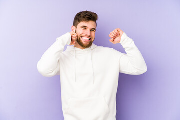 Young caucasian man isolated on purple background dancing and having fun.