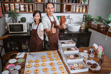 smiling young couple in modern kitchen with thumbs up in front of a donut on a table