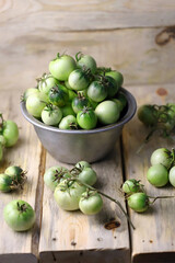 Green tomatoes in a bowl on a wooden surface. Rustic style. Selective focus. Macro.
