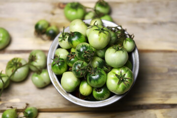 Green tomatoes in a bowl on a wooden surface. Rustic style. Selective focus. Macro.