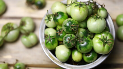Green tomatoes in a bowl on a wooden surface. Rustic style. Selective focus. Macro.