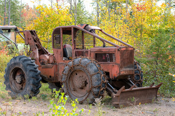 Obraz premium Abandoned Heavy Tractor With Plow On Front. An old, rusty, abandoned heavy tractor with a plow on the front. The tractor is next to a woods. Chains on front tires. No identifying markings.