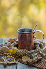 Copper mug with hot tea on a wooden table with autumn leaves. Retro style photo
