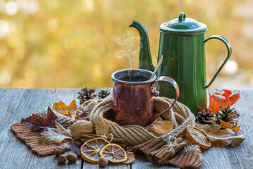 A copper mug with hot coffee and a coffee pot on a wooden table with autumn leaves, on an autumn...