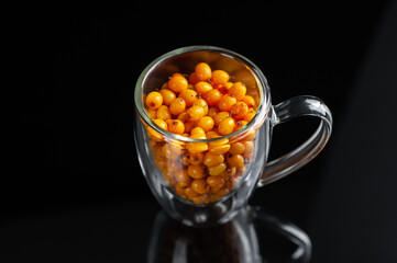 sandthorn berries in a transparent mug on a black background