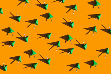 green push pins on a bright orange background. School and office supplies top view. Colorful background