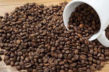 Coffee beans spilled from a cup on a wooden table.