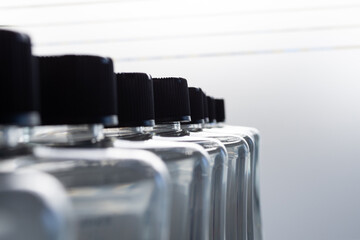 New clear plastic bottles with clear liquid inside. The bottle is closed with a black stopper or cork. Bottles stand in a row one after another on a gray background. Close-up