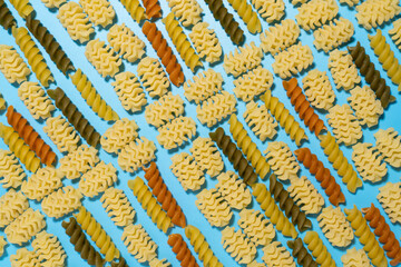 Raw colored fusilli and radiatori type of pasta on blue  background.