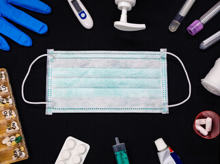 Close-up of centered green medical or surgical mask on black background. Around the mask are various medical supplies. Тhe concept of medical supplies for personal protection and treatment coronavirus