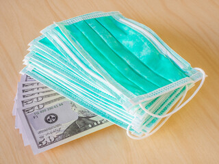 A lot of medical surgical green color masks on fan-shaped american money banknotes isolated on wooden surface background. The concept of medical supplies accessories for personal protection. Close-up