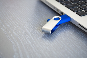 Blue USB flash drive inserted or connected to laptop computer's USB port. Notebook is on a light gray desk background.  Data storage and modern electronics concept. Close-up.