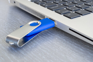 Blue USB flash drive inserted or connected to laptop computer's USB port. Notebook is on a light gray desk background.  Data storage and modern electronics concept. Close-up.