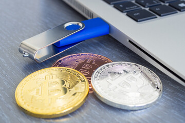 Blue USB flash drive inserted or connected to laptop computer's USB port. Notebook is on a light gray desk background. Bitcoin coins are nearby.  Data storage and modern electronics concept. Close-up.