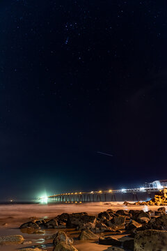 Richfield Pier behind rocky shore sand of Mussel Shoals beach with shooting stars in sky above.