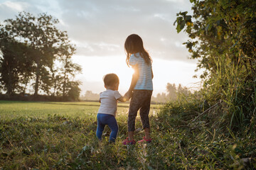 older sister plays with her younger sister in the fields on sunset