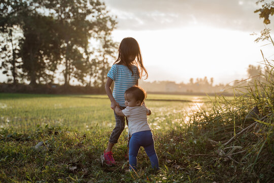 older sister plays with her younger sister in the fields on sunset