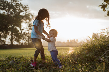 older sister plays with her younger sister in the fields on sunset