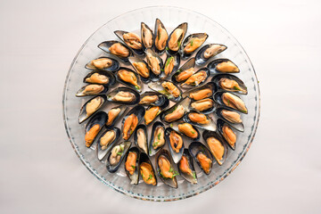 Mussels cooked with onion and herbs served on a round glass plate, gray background with copy space, high angle view from above