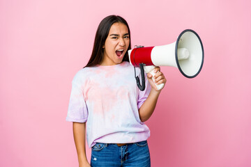 Young asian woman holding a megaphone isolated on pink background screaming very angry and aggressive.