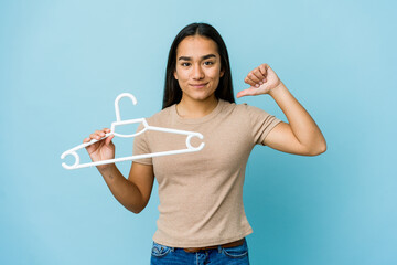 Young asian woman holding a hanger isolated on blue background feels proud and self confident, example to follow.