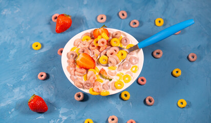 Healthy breakfast with cereal and berries. From above of bowl with delicious healthy breakfast made with colorful cereal rings and fresh strawberry with milk served on blue table