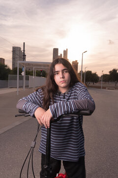 Teenager with long hair or girl posing with her bike or scooter at sunset.