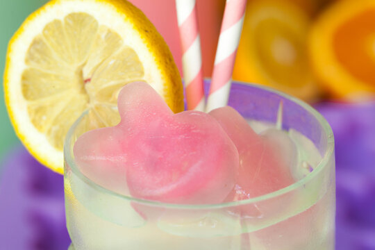 Bunny Shaped Frozen Fruit Pink Lemonade Ice Cubes In Glass With Pink And White Striped Straws With Lemon Round Garnish