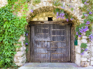 Old wooden doors of an old stone house covered by purple flowers in the typical village of La...