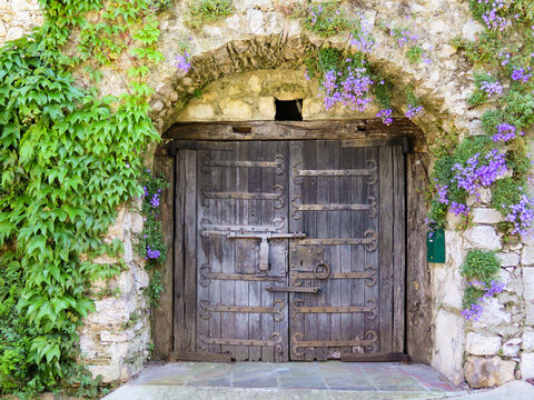 Fototapeta Old wooden doors of an old stone house covered by purple flowers in the typical village of La Turbie in provence 