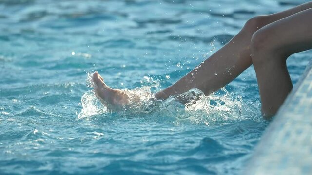 Cheery boy`s legs doing bike actions hit water in a wading pool in slow motion