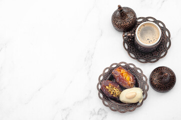 Fototapeta na wymiar Ramadan sweets, eid mubarak and luxurious desserts concept with stuffed dates on metal plate and small coffee cup isolated on white marble background with copy space