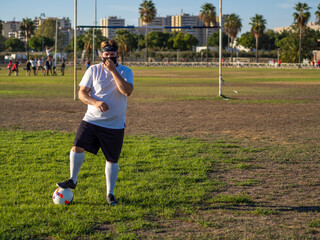 Hombre gordo posando en un campo de futbol vistiendo mascarilla 