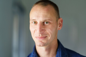 Front view close up portrait of male adult caucasian man with short blonde hair and green eyes standing at home in day looking to the camera smiling with copy space