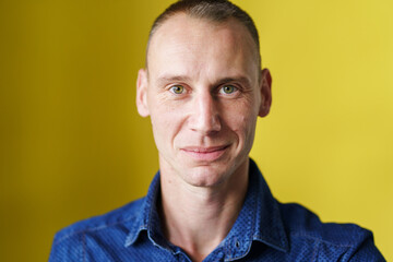 Fototapeta premium Front view close up portrait of male adult caucasian man with short blonde hair and green eyes in front of yellow background looking to the camera smiling with copy space
