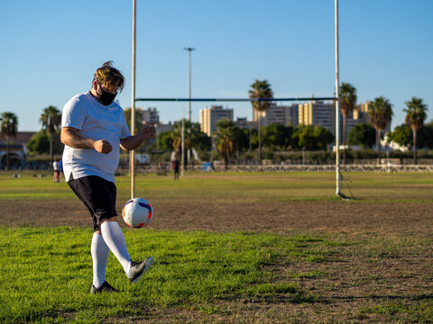 Hombre gordo con mascarilla entrenando y jugando al futbol 