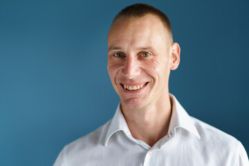 Fototapeta premium Front view close up portrait of male adult caucasian man with short blonde hair and green eyes in front of blue background looking to the camera smiling with copy space