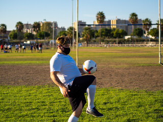 Hombre gordo con mascarilla entrenando y jugando al futbol 