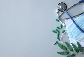 Composition with medical stethoscope, disposable face mask pills on gray background near the plant. View from above. Free copy space
