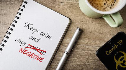 Covid-19 - stay negative. Flat lay. Work area with notepad, pen, cell phone and a cup of coffee. 