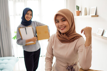 attractive cheerful young muslim business woman working on laptop and smiling while sitting at her desk modern office with her friend hold package at studio