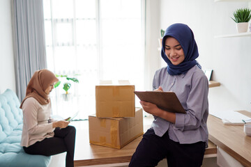 attractive cheerful young muslim business woman working on laptop and smiling while sitting at her desk modern office with her friend at studio